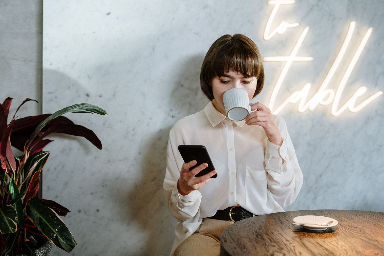 Kvinne på kafé som drikker kaffe og ser på mobilen