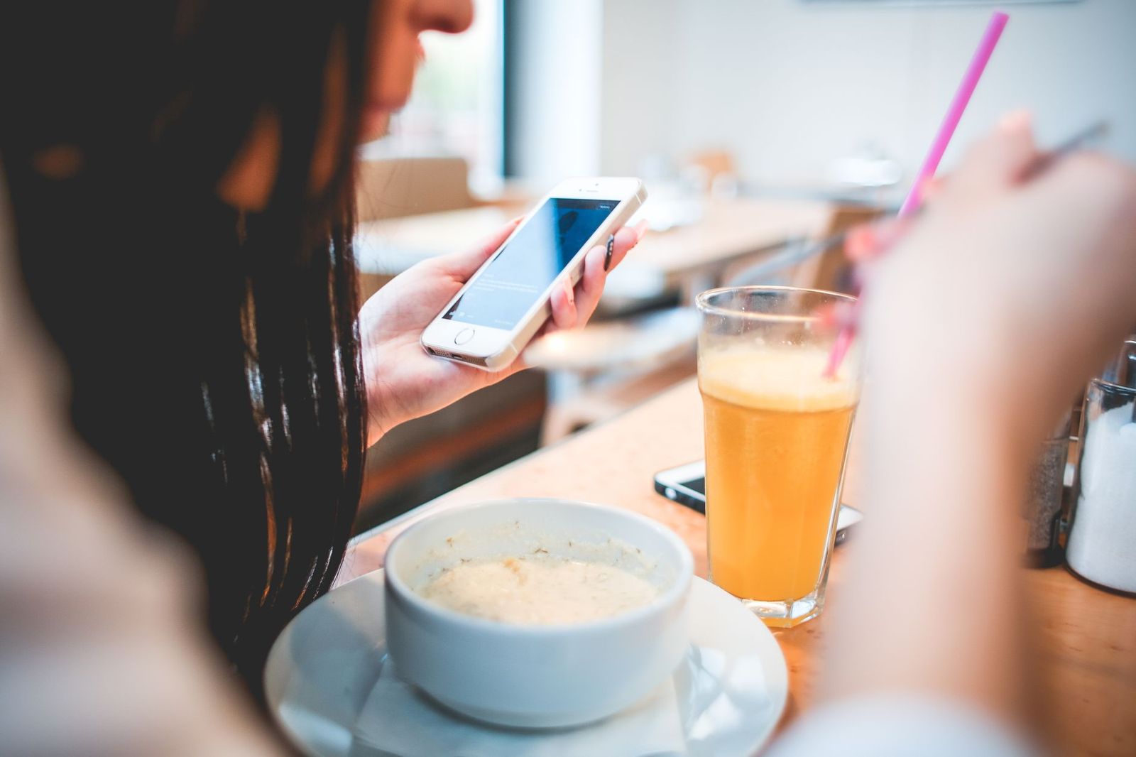 Kvinne på kafé som ser på mobilen, med et glass appelsinjuice på bordet
